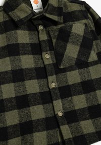 Grön- och svartrutigt flanellskjorta med krage, knappstängning fram och bröstficka. Tillverkad av mjukt, texturerat tyg.