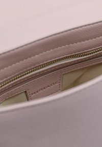 Lys pink lædertaske indvendigt med cremefarvet foring, der har en lynlåslomme og brandmærke prægede på læderet.
