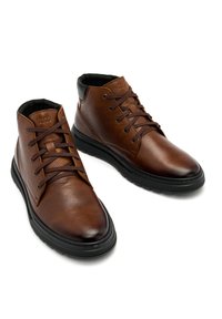 Brązowe skórzane buty chukka z teksturowaną powierzchnią, czarnymi akcentami, sześcioma otworami na sznurowadła i gumowymi podeszwami dla lepszej przyczepności.