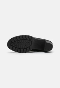 Suela de zapato negra con una superficie de goma texturizada. Presenta surcos en la suela y un talón reforzado. Diseño minimalista sin marcas visibles.