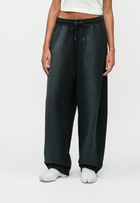 Σκούρο γκρι φαρδιά παντελόνια φόρμας με ελαστική μέση και κορδόνι, διαθέτοντας μαλακή υφή και πλάγιες σχισμές στο στρίφωμα.