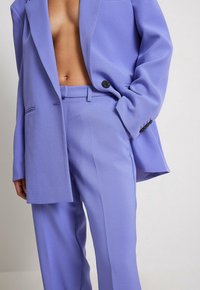 Lavendel Zweiteiler aus strukturiertem Stoff; umfasst ein tailliertes Blazer mit einem einzelnen Knopf und passende Hose mit dezenten Falten.