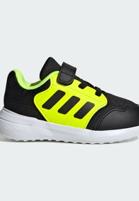 Black and neon yellow athletic shoe with a textured mesh upper, three black stripes, and a hook-and-loop strap over the laces. White sole.