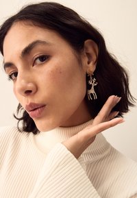Gold-tone earrings featuring a reindeer design adorned with clear rhinestones and a red accent, set against a bare background.