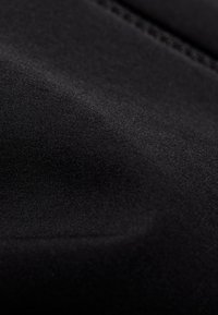 Gros plan sur un tissu noir lisse avec des coutures fines et une texture subtile, montrant des plis et des contours doux.