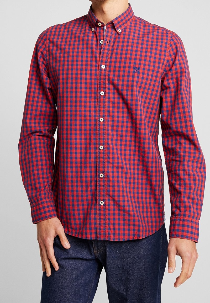 Camicia a righe rossa e blu con bottoni, maniche lunghe, chiusure a bottone bianche e un piccolo logo sul lato sinistro del petto. Tessuto di cotone.