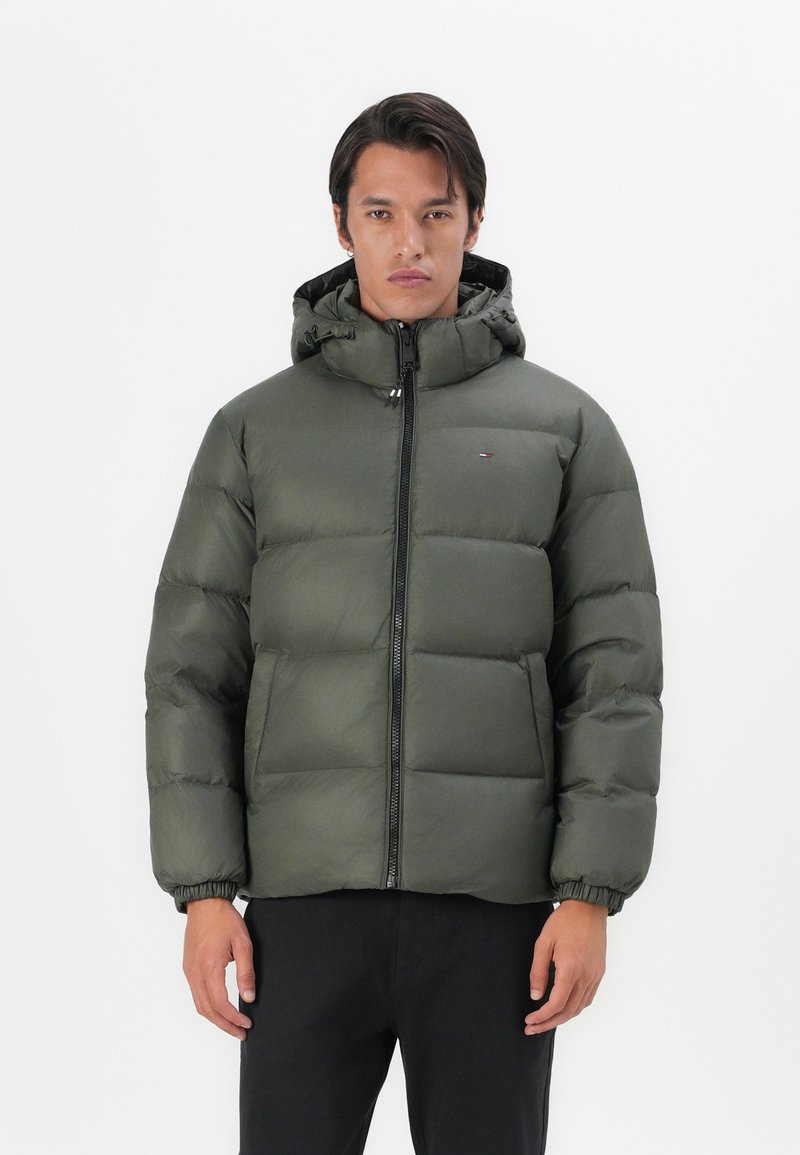Groene pufferjack met een ritssluiting aan de voorkant, elastische manchetten en een capuchon. Het materiaal heeft een glanzende textuur, met een klein logo op de borst.