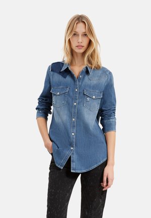 Denimskjorte med en lys til mørkeblå gradient, knaplukning, to brystlommer og lange ærmer. Slidte detaljer på skuldrene.
