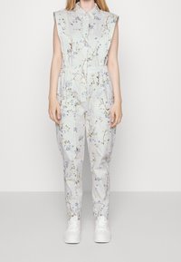 Floral-patterned jumpsuit in light blue fabric, sleeveless design, with a collar and elastic waist. Paired with white sneakers.