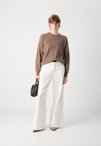 Καφέ πλεκτό πουλόβερ, λευκά παντελόνια με φαρδύ ποδαράκι, μαύρη πλεγμένη τσάντα και μαύρες γόβες. Μινιμαλιστικός σχεδιασμός με απαλά υφάσματα και καθαρές γραμμές.