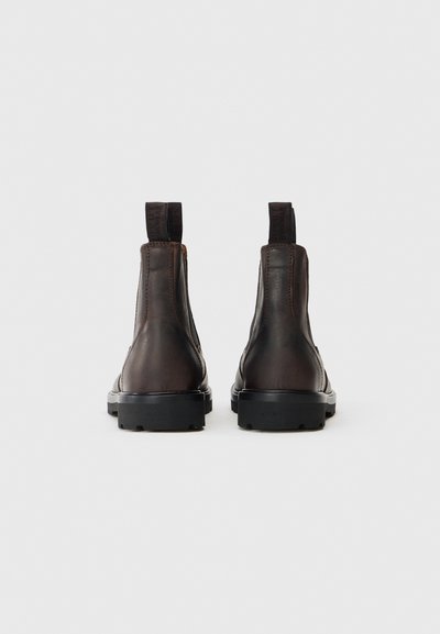 Botas de tornozelo em pele castanha com uma textura suave, painéis laterais elásticos e puxadores; apresentando uma sola robusta em borracha preta.
