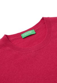Maglione rosso a maglia con scollatura rotonda. Presenta un'etichetta verde con la scritta "UNITED COLORS OF BENETTON." Texture morbida con una finitura liscia.