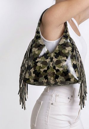 Schoudertas met groen camouflagepatroon en lange franjes gedragen door een persoon in een witte tanktop en broek tegen een effen achtergrond.