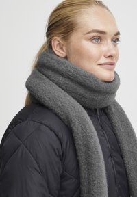 Grå ullskjerf med en myk tekstur, svøpt rundt halsen, kombinert med en svart boblejakke. Jevn finish, varm og koselig utseende.