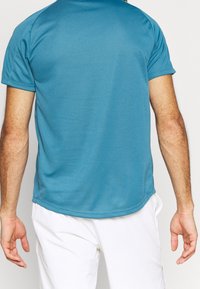 Modrá sportovní košile s krátkým rukávem vyrobená z hladkého, vlhkost-odpudivého materiálu, s kulatým lemem a pohodlným střihem.