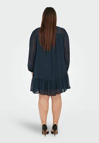 Mörkblå chiffongklänning med långa ärmar, horisontella randiga mönster och en volangkant. Bärs med svarta högklackade skor.