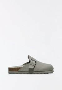 Sabot en daim gris à enfiler avec une grande bride à boucle et une semelle texturée pour une bonne adhérence, présenté sur un fond blanc uni.