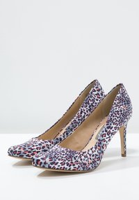 Vysoce podpatek s špičatou špičkou v lesklé bílé barvě s vícolorním leopardím vzorem. Stiletto podpatek, hladká textura.