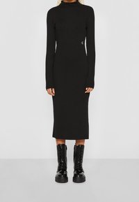 Abito lungo nero a righe con maniche lunghe, colletto alto, design aderente e dettaglio del logo laterale; abbinato a stivali neri lucidi con lacci.