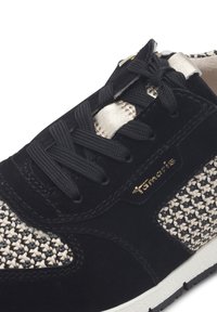 Sneaker nera in suede con texture intrecciata beige sul lato, lacci neri e dettagli dorati sulla linguetta. Suola in gomma leggera per il comfort.
