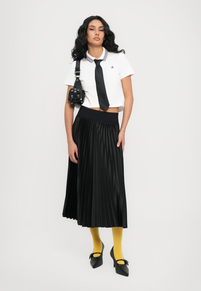 Hvid cropped polo shirt med flerfarvet krave, sort slips, sort plisseret maxiskirt, gul strømpebukser, sorte spidse sko med sløjfedetalje.