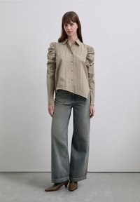 Rutet beige og brun skjorte med puffede ærmer, knaplukning, asymmetrisk kant, kombineret med vidde jeans og brune ankelstøvler med hæl.