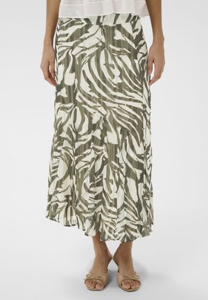 Femme portant une jupe midi plissée à imprimé zèbre vert et blanc, avec des escarpins beiges à bouts ouverts et un chemisier blanc orné de dentelle.