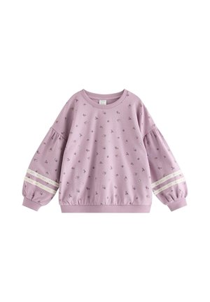 Young girl stands smiling wearing matching lilac floral sweatshirt and pants with lace stripes and matching hair tie.