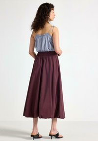 Lys blå ærmeløs top med smock-detaljer og justerbare stropper, parret med en lang, svævende maroon nederdel, der bæres med sorte åbne sandaler.