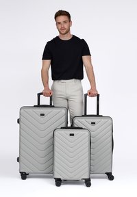 Trois valises rigides grises avec un motif en chevron, de tailles variées, dotées de poignées noires et de roues pour la mobilité.