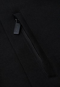 Zwarte ritszak op textuurstof, met een gladde ritstrekkertje met het label "OMBRE." Close-up afbeelding benadrukt de materiaalkenmerken en het design.