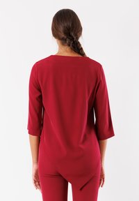 Top borgogna con maniche a tre quarti, caratterizzato da un collo rotondo e un orlo asimmetrico per una silhouette fluida. Tessuto dalla texture liscia.