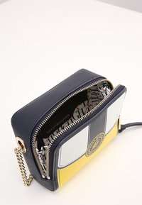 Navy faux leather crossbody bag with yellow, white, and black sections; gold hardware; zip closure; patterned interior lining featuring logo.
