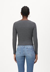 Top gri cu mâneci lungi, cu un design ajustat, asortat cu blugi skinny albaștri, având buzunare la spate și talie medie. Textura țesăturii este simplă.