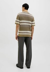 Polo a maniche corte in maglia con un motivo a righe testurizzate nei toni del beige, crema e marrone; abbinato a pantaloni grigi larghi e scarpe nere.