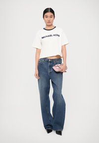 T-shirt bianco corto con colletto blu navy, logo "MICHAEL KORS"; jeans in denim blu larghi; borsa a mano rosa; décolleté nere a punta.