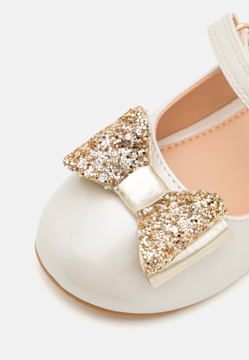Hellbeige, patentierte Ballettschuhe aus Leder mit einer großen goldenen Glitzer-Schleife und einem metallischen Riemen. Rundliche Zehenform mit einem weichen Innenfutter.