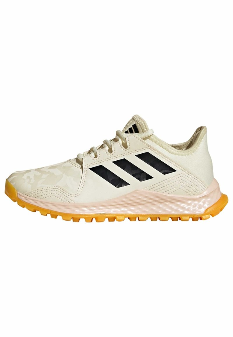 Chaussure de sport beige clair avec une tige texturée, trois rayures noires et une semelle en caoutchouc orange contrastante. Dotée d'un design à lacets.