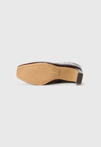 Bota de cuero marrón tumbada de lado mostrando una suela color crema con detalle de costura en forma de triángulo y el texto "dolce vita" cerca del talón.