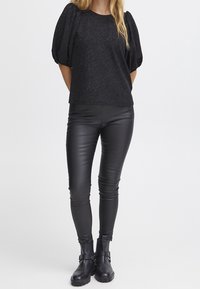 Top nero in tessuto testurizzato con maniche a sbuffo, abbinato a pantaloni in pelle nera aderenti e stivaletti. Design elegante e minimalista nel complesso.