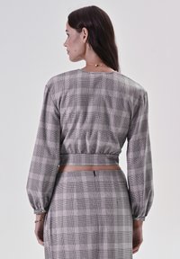 Top corto a quadri grigio con maniche lunghe e vita elastica, abbinato a una gonna a vita alta coordinata con un dettaglio zip sottile.