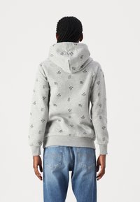 Szara bluza z kapturem o miękkiej teksturze, z wzorem małych czarnych kwiatowych motywów, regulowany kaptur i ściągacze na rękawach. W połączeniu z niebieskimi dżinsami.