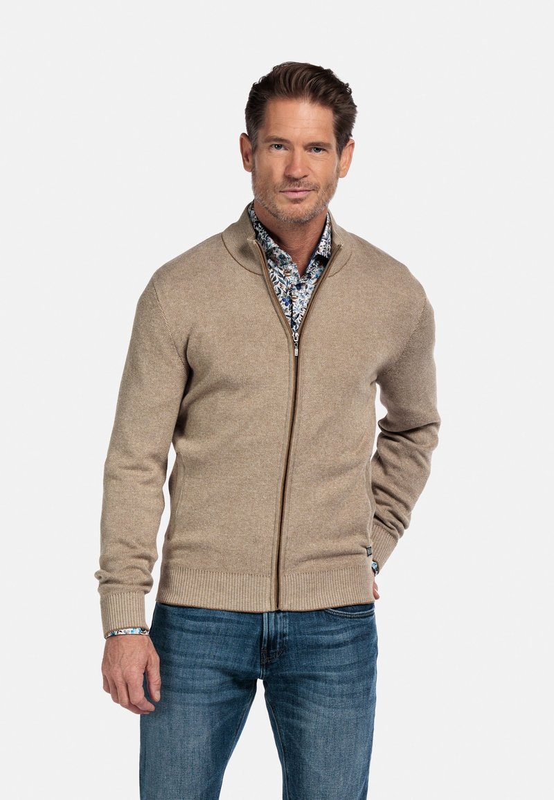 Beige zip-up trui met geribbelde boorden en onderrand, gedragen over een patroondem blauwe shirt, gecombineerd met blauwe jeans. Glad textuur en casual ontwerp.