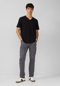 Czarny t-shirt z dekoltem w serek i krótkim rękawem, połączony z jasnoszarymi spodniami. Białe trampki z czarnymi akcentami. Gładki, swobodny design.