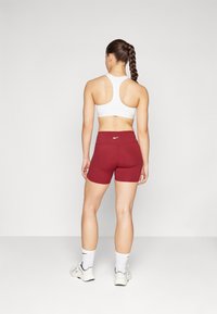 Fehér sportmelltartó és bordó rövidnadrág Nike logóval, sima felület, testhez simuló fazon, fehér sportzoknikkal és cipőkkel párosítva.