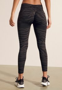 Svarta och grå tigerrandiga leggings med hög midja och textilstruktur, ihop med svarta träningsskor på en neutral golvyta.
