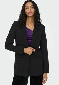 Veste noire ajustée avec revers crantés, fermeture à un bouton et deux poches avant. Texture de tissu lisse, design cintré.