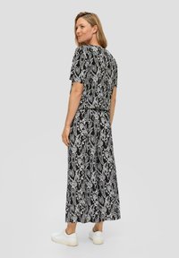 Schwarz-weiß gemustertes Maxikleid mit kurzen Ärmeln, das ein Blumenmuster aufweist. Knielange Länge, kombiniert mit weißen Sneakern.