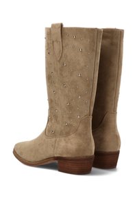 Botas de ante beige hasta la rodilla con punta redonda, adornadas con tachuelas plateadas y un tacón bajo apilado. Incluyen una lengüeta para facilitar su uso.