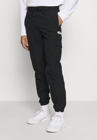 Svarte joggerbyxor med resår i midjan, sidfickor och en cargoficka; har vita logotypdetaljer och en avsmalnande benform.